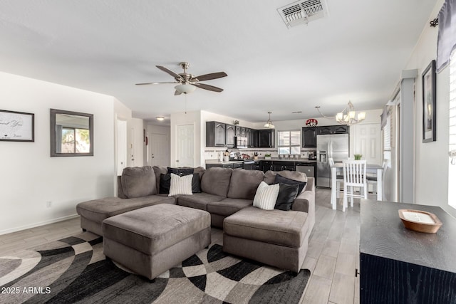 living area with light wood-style floors, baseboards, visible vents, and ceiling fan with notable chandelier