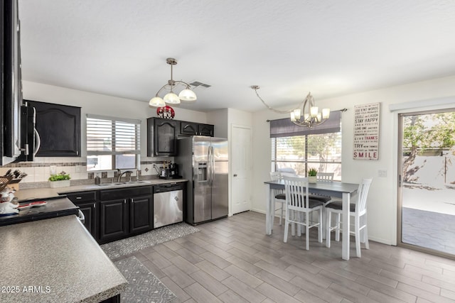 kitchen with a sink, visible vents, appliances with stainless steel finishes, light wood-type flooring, and decorative backsplash