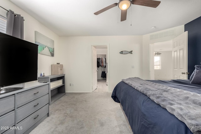 bedroom featuring a walk in closet, light colored carpet, ceiling fan, and baseboards