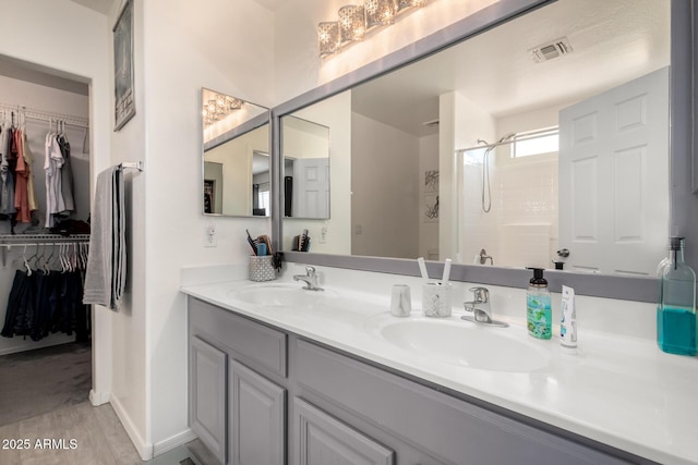 full bath featuring double vanity, a stall shower, a sink, and a walk in closet