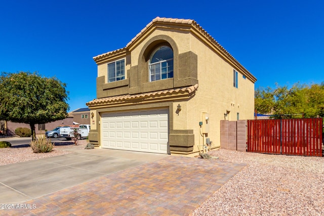 mediterranean / spanish-style home with a garage, driveway, fence, and stucco siding