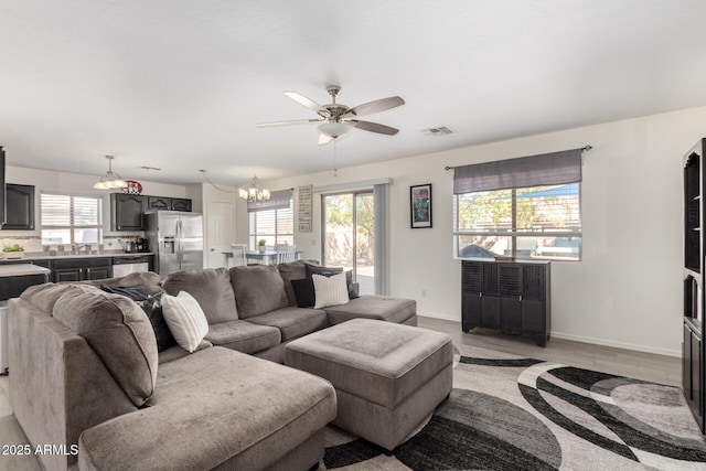 living room with a healthy amount of sunlight, visible vents, baseboards, and ceiling fan with notable chandelier