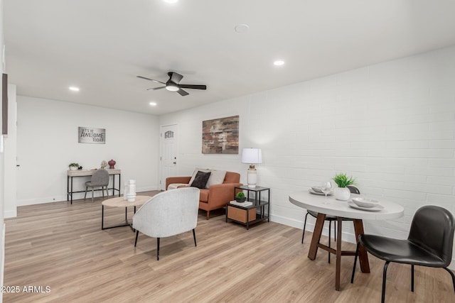 living room with light hardwood / wood-style flooring, ceiling fan, and brick wall