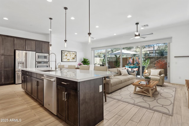 kitchen with appliances with stainless steel finishes, ceiling fan, sink, decorative light fixtures, and a center island with sink