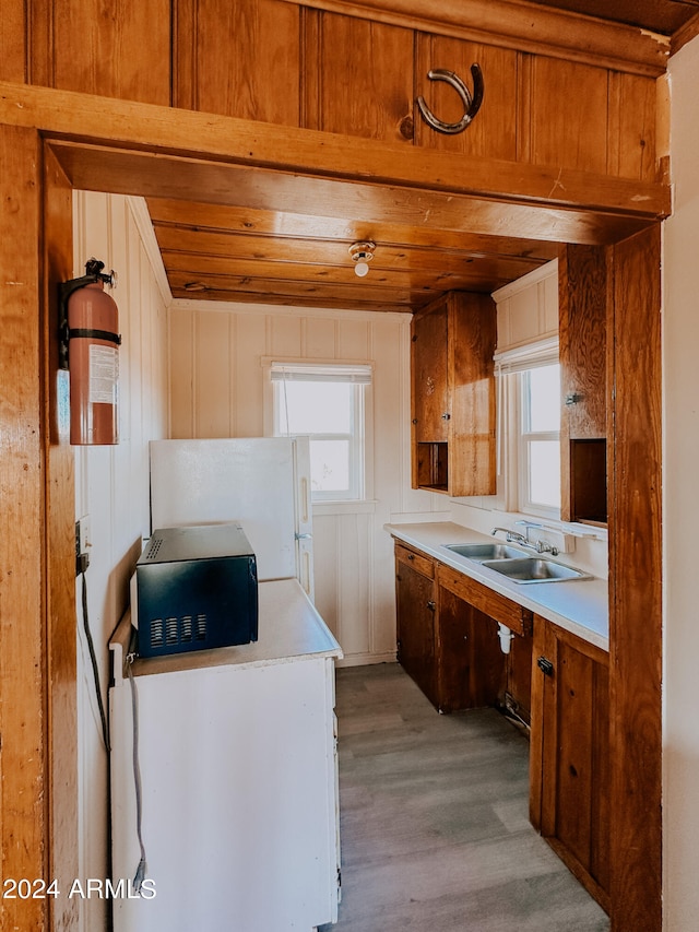 kitchen with fridge, wooden walls, light hardwood / wood-style flooring, and sink