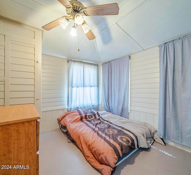 bedroom with ceiling fan, wood walls, and concrete flooring