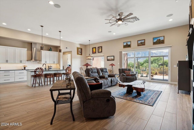 living room featuring light hardwood / wood-style flooring, ceiling fan with notable chandelier, and sink