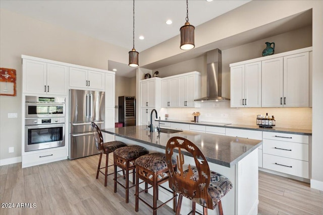 kitchen featuring sink, an island with sink, a kitchen bar, wall chimney range hood, and appliances with stainless steel finishes