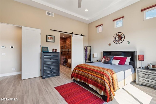 bedroom with light hardwood / wood-style flooring, connected bathroom, ceiling fan, and a barn door