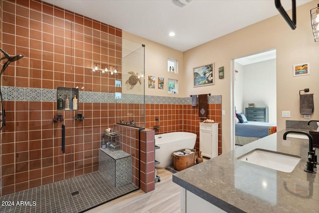 bathroom with tile walls, wood-type flooring, independent shower and bath, and vanity