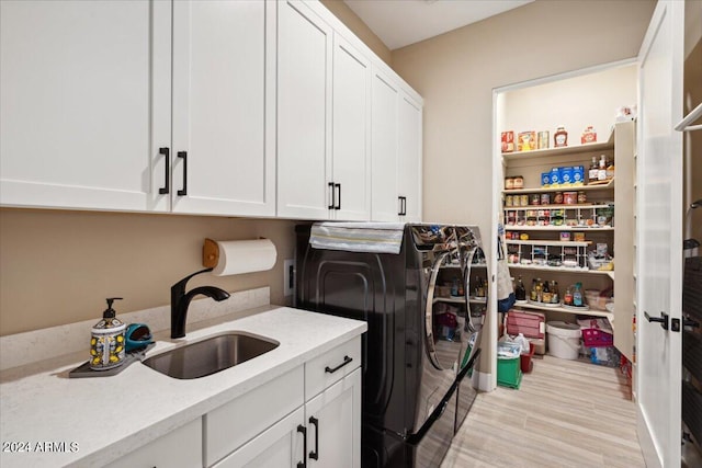 clothes washing area featuring light wood-type flooring, sink, washer and dryer, and cabinets