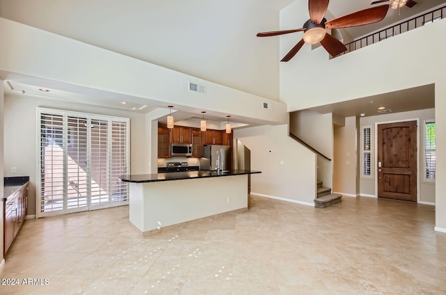 kitchen featuring a kitchen island, stainless steel appliances, a high ceiling, ceiling fan, and decorative light fixtures