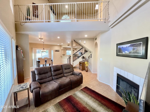 tiled living room featuring stairway, arched walkways, a towering ceiling, and a tiled fireplace