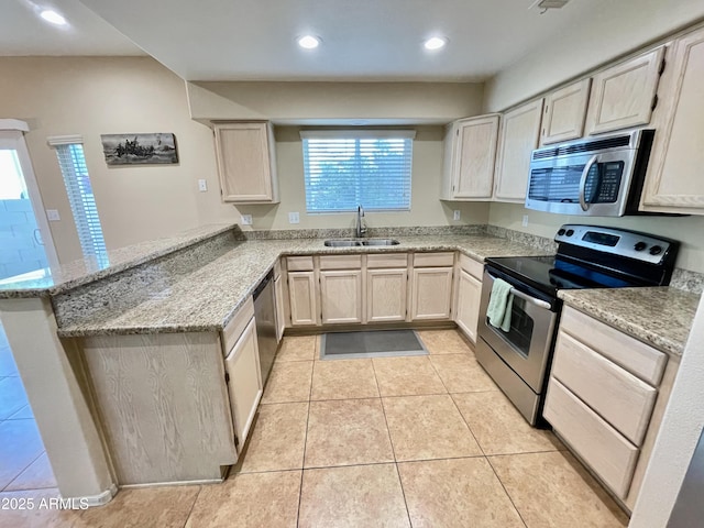 kitchen with a sink, light stone counters, appliances with stainless steel finishes, a peninsula, and light tile patterned floors