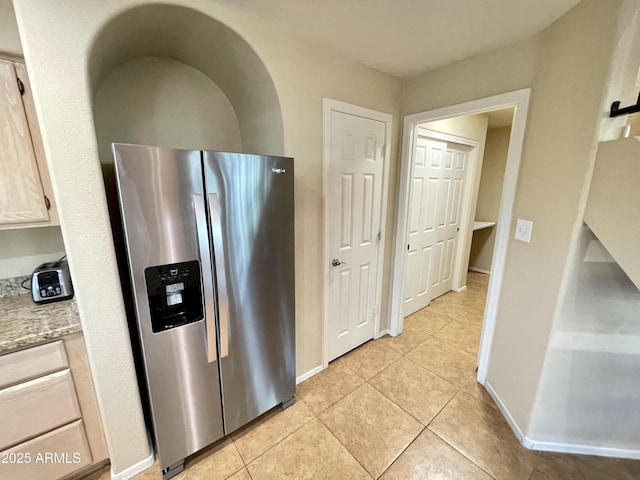 kitchen with light tile patterned flooring, baseboards, and stainless steel refrigerator with ice dispenser