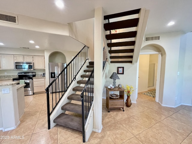 staircase featuring arched walkways, visible vents, tile patterned flooring, and recessed lighting