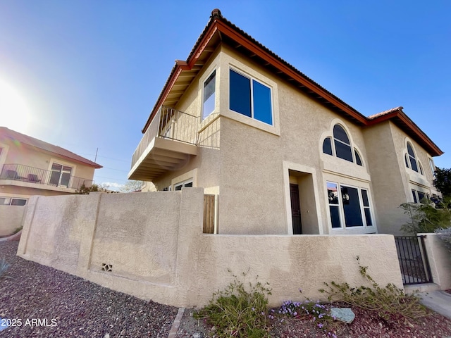 view of home's exterior featuring a balcony, a gate, fence, and stucco siding