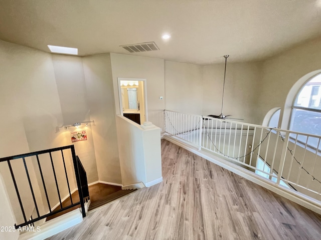 corridor featuring an upstairs landing, visible vents, baseboards, and wood finished floors