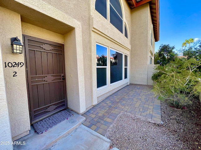 view of exterior entry featuring stucco siding and a patio