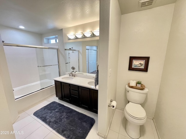 bathroom featuring visible vents, bath / shower combo with glass door, toilet, double vanity, and tile patterned floors