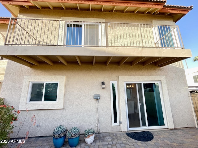 rear view of house with a patio, a balcony, and stucco siding