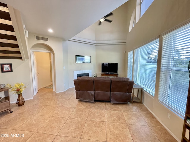 living area featuring visible vents, a ceiling fan, arched walkways, light tile patterned floors, and a tile fireplace