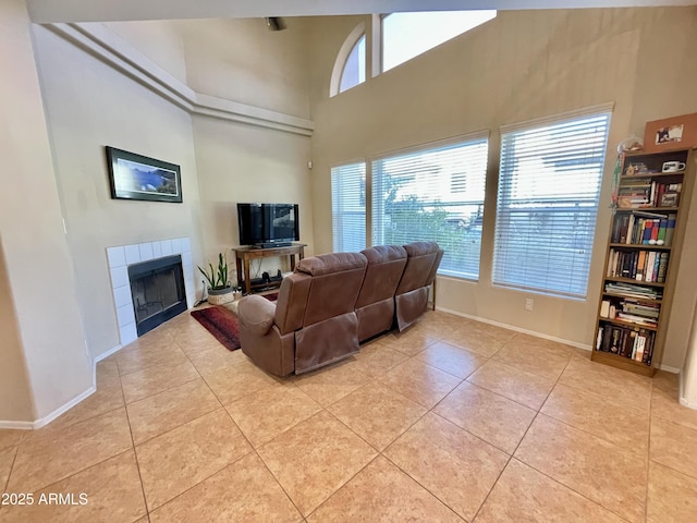 living area featuring a high ceiling, light tile patterned flooring, baseboards, and a tile fireplace