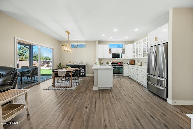 kitchen with white cabinetry, appliances with stainless steel finishes, hanging light fixtures, and hardwood / wood-style flooring