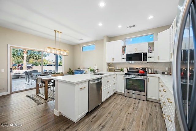 kitchen with white cabinetry, stainless steel appliances, kitchen peninsula, and hanging light fixtures