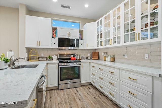 kitchen featuring sink, white cabinets, decorative backsplash, stainless steel appliances, and light stone countertops