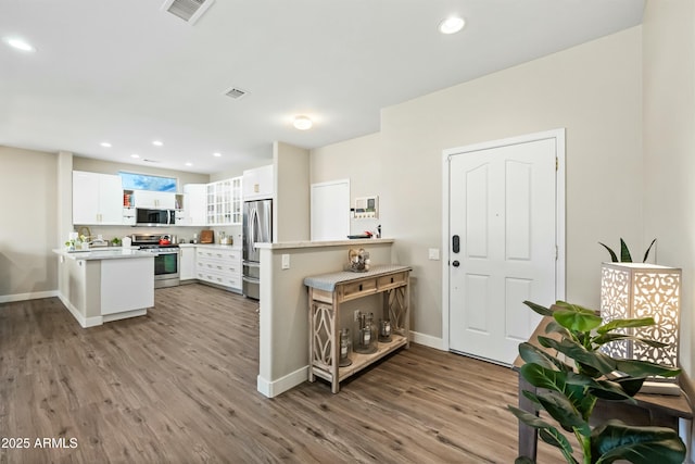 kitchen with white cabinetry, appliances with stainless steel finishes, kitchen peninsula, and hardwood / wood-style floors