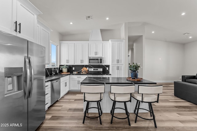 kitchen featuring a kitchen breakfast bar, appliances with stainless steel finishes, backsplash, white cabinets, and a kitchen island