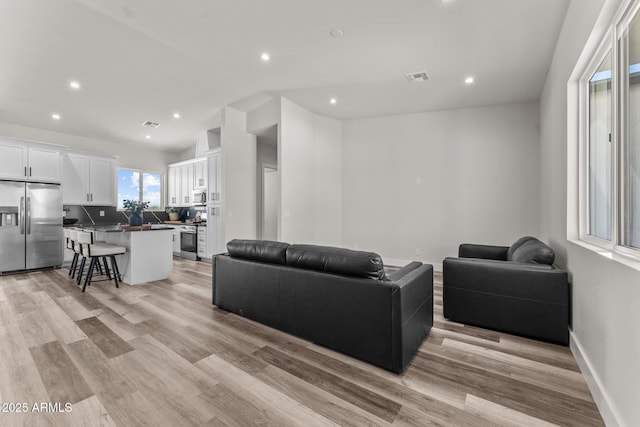 living room with baseboards, light wood-type flooring, visible vents, and recessed lighting