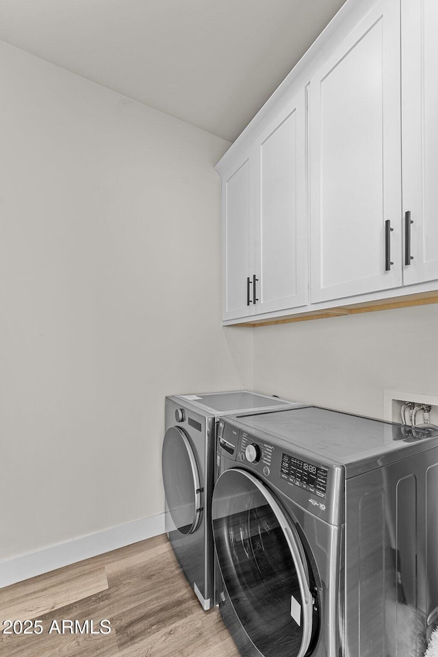 clothes washing area featuring light wood-type flooring, washer and clothes dryer, and cabinets