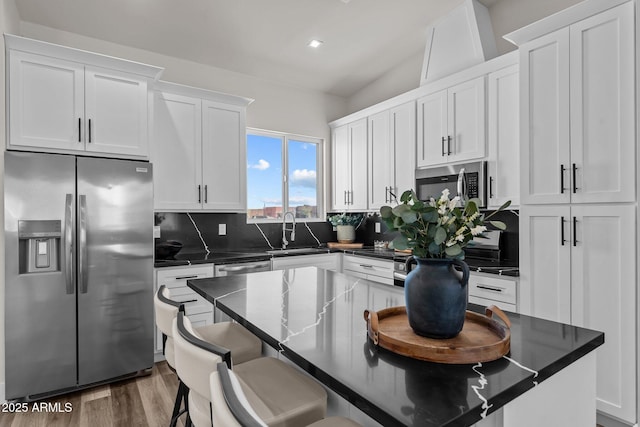 kitchen with appliances with stainless steel finishes, sink, backsplash, white cabinetry, and a center island