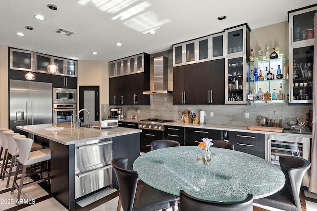 26036 N 85th Dr, Peoria, AZ 85383 - kitchen with built in appliances, wall chimney exhaust hood, an island with sink, a breakfast bar, and backsplash