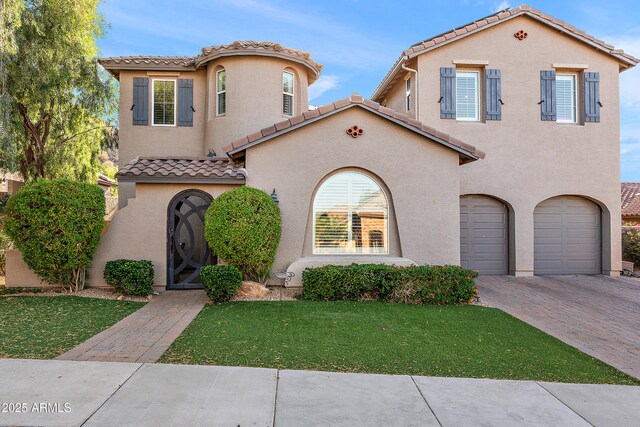 26036 N 85th Dr, Peoria, AZ 85383 - mediterranean / spanish house featuring an attached garage, a tile roof, decorative driveway, stucco siding, and a front yard