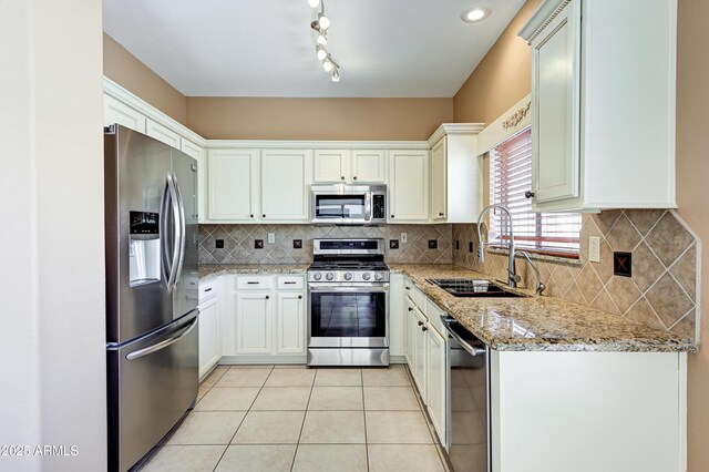 kitchen featuring light stone counters, light tile patterned floors, a sink, decorative backsplash, and appliances with stainless steel finishes