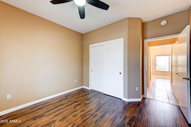 unfurnished bedroom featuring a ceiling fan, baseboards, a closet, and dark wood-style flooring
