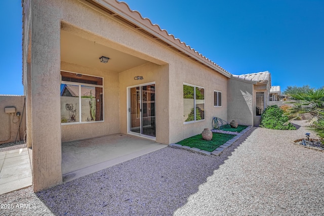 back of house with stucco siding, a tiled roof, and a patio
