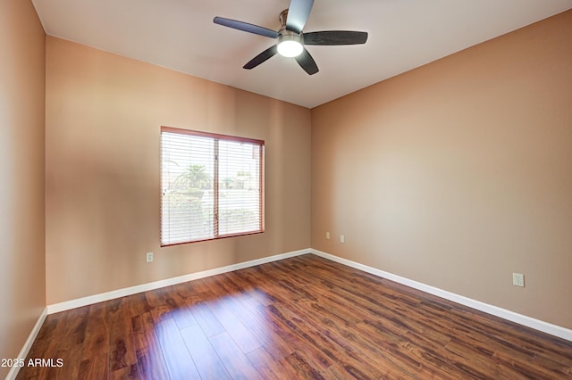 spare room featuring dark wood-type flooring, a ceiling fan, and baseboards
