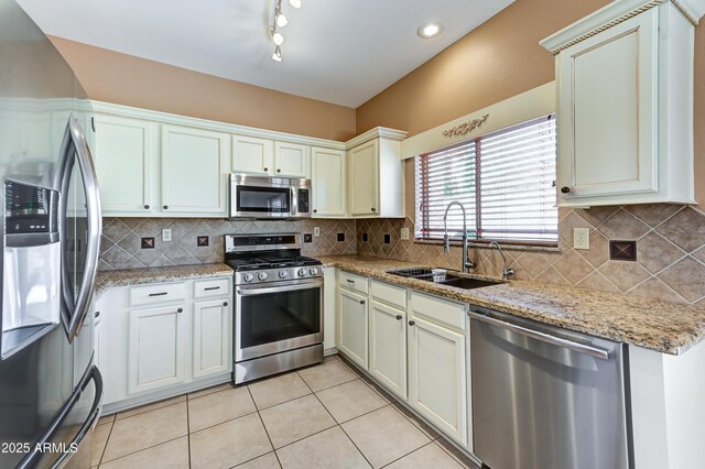 kitchen featuring stainless steel appliances, a sink, light tile patterned flooring, decorative backsplash, and light stone counters