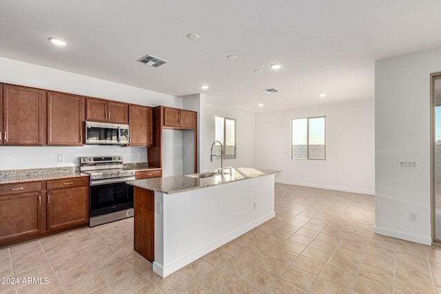 kitchen with a kitchen island with sink, sink, light tile patterned floors, light stone countertops, and appliances with stainless steel finishes