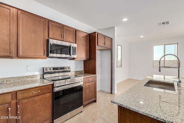 kitchen with light tile patterned floors, light stone countertops, sink, and appliances with stainless steel finishes