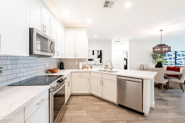 2511 W Queen Creek Rd Unit 325, Chandler, AZ 85248 - kitchen with appliances with stainless steel finishes, a peninsula, decorative backsplash, white cabinetry, and a chandelier