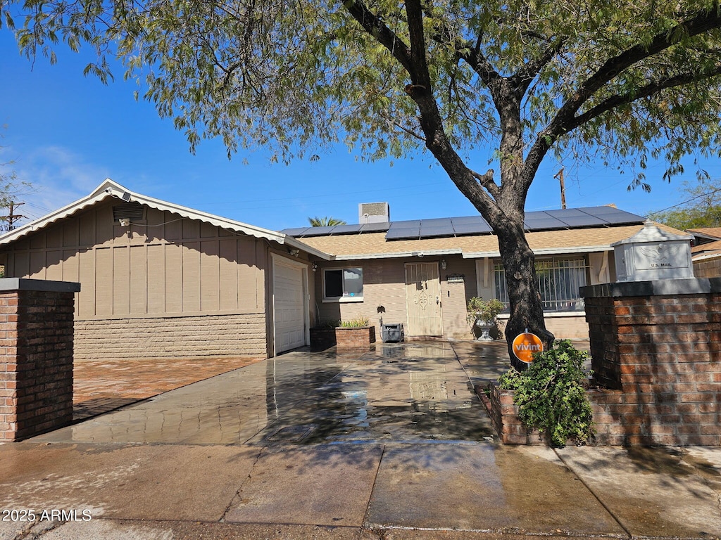 single story home featuring brick siding, solar panels, board and batten siding, a garage, and driveway