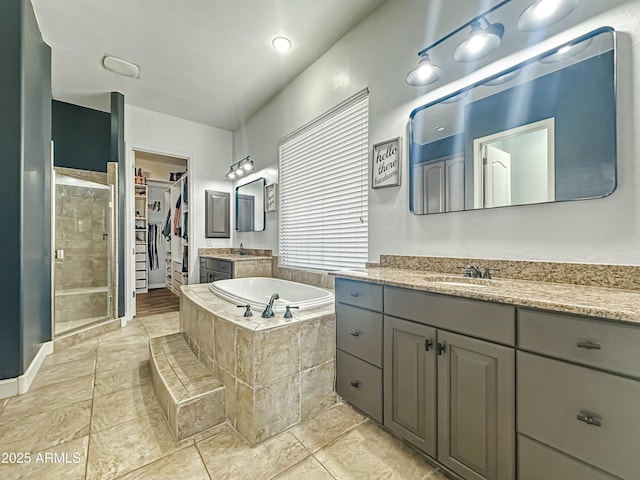 bathroom featuring a walk in closet, a garden tub, two vanities, a sink, and a shower stall