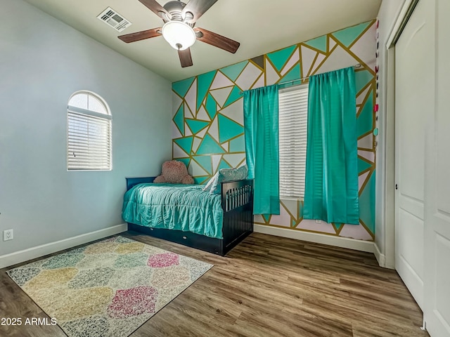 bedroom with an accent wall, wood finished floors, visible vents, and baseboards