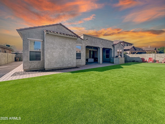 back of house at dusk featuring a patio, fence, a lawn, and stucco siding