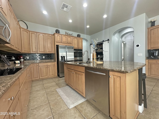 kitchen with arched walkways, a kitchen island with sink, stainless steel appliances, visible vents, and tasteful backsplash